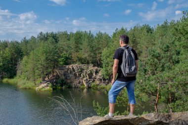 Sırt çantası ile üst düzey bir beyaz adam kayanın üzerinde duruyor ve gölde görünüyor