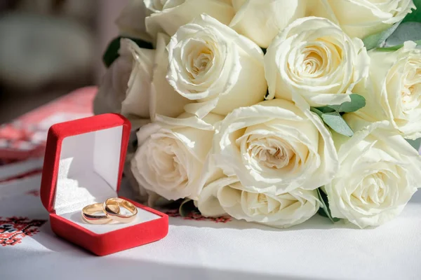 Two rings in the red box and wedding bouquet on the table. Closeup view