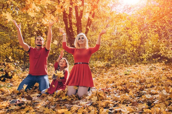 Beautiful young happy family throwing leaves in autumn day.