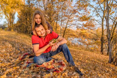 Genç baba ve sonbahar yaprakları üzerinde oturan ve having fun sonbahar parkta Nehri yakınında şirin küçük kızı sakallı. Ebeveynlik kavramı ve mutlu bir aile. 