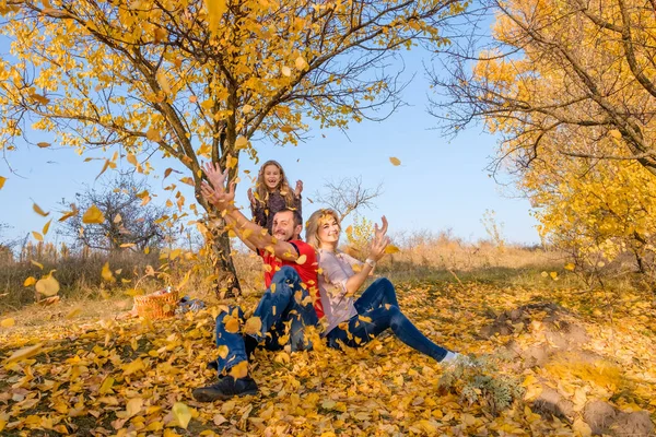 Beautiful young white family throwing leaves in sunny cloudless autumn day. Concept of happy family relations, parenting, joyful childhood.
