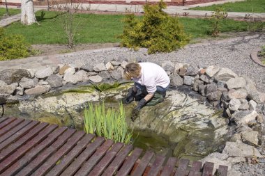 Kadın Bahçe gölet temizler. DIY balık pond bakımı üzerinde mevsimlik çalışma