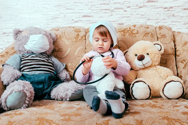 Очаровательный милый ребенок в одежде доктора, осматривающего игрушку в доме — стоковое фото