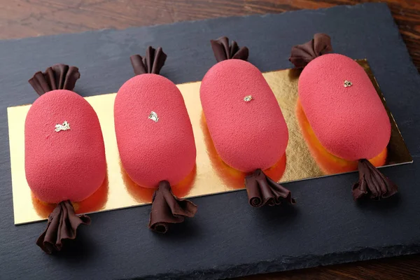 Four red  mini mousse cakes in shape of candy on dark stone plat