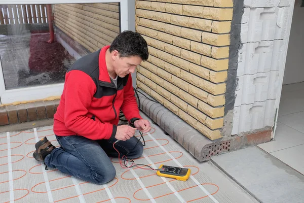 Electrician installing heating electrical cable on concrete floor. Man measure resistance of cable.