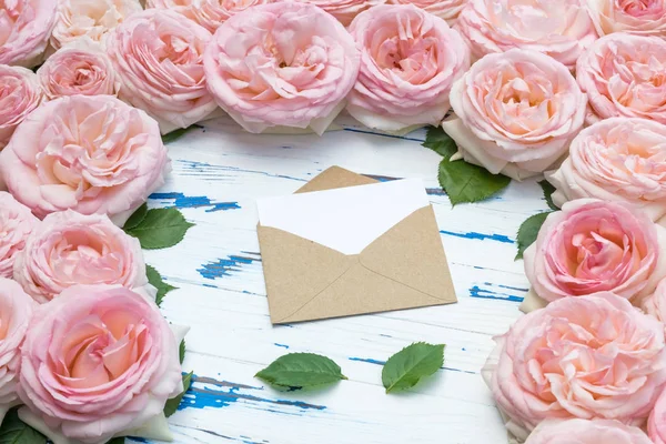 Flowers composition. Open envelope in the frame made of pink roses on aged wooden background. — Stock Photo, Image
