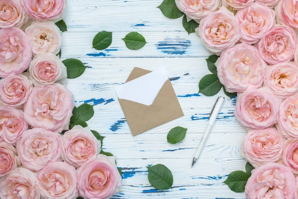 Composición de flores. Sobre de papel artesanal abierto y bolígrafo en el marco de rosas rosadas sobre fondo de madera envejecida . — Foto de Stock