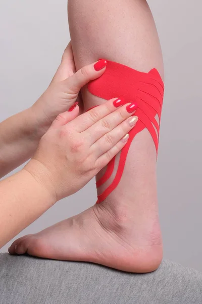 Manos del fisioterapeuta médico aplicando cinta de kinesio en el primer plano de la pierna de la mujer . — Foto de Stock