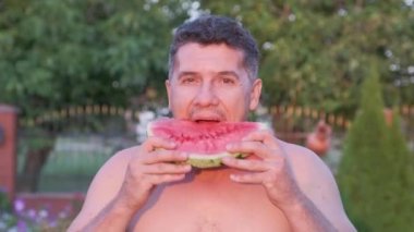 Yakışıklı orta yaşlı adam sulu bir karpuz açık yiyor. yakın çekim görünümü