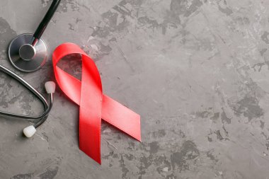Beton bir arka planda kırmızı kurdele ve steteskop. 1 Aralık Dünya Yardım Günü, HIV hastalığı kampanyası.
