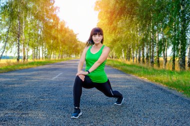 Kırsalda asfalt yolda koşmadan önce bacaklarını esneten beyaz bir kadın, kaslar için ısınıyor.. 