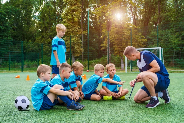 Genç koç küçük çocuklara futbol sahasında oynama stratejisini öğretiyor.. — Stok fotoğraf