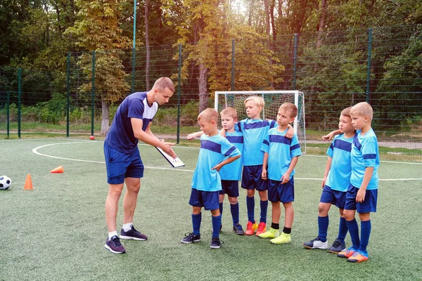 Молодий тренер навчає маленьких дітей стратегії гри на футбольному полі . — стокове фото