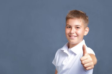Yakışıklı, gülümseyen, beyaz bir çocuk. Gri üzerinde baş parmağıyla işaret ediyor.