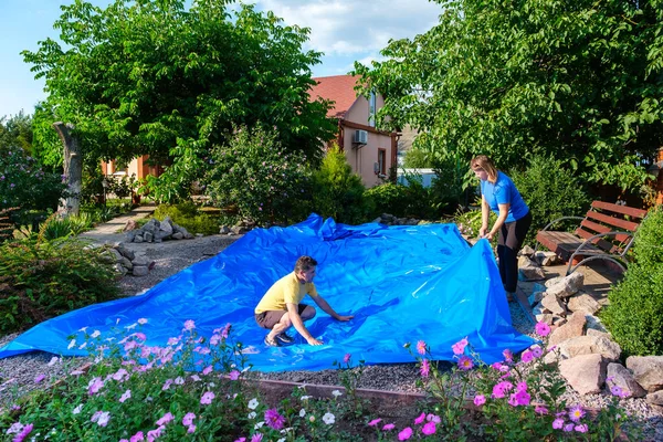 Rodzina kładzie niebieską folię HDPE na ziemi, aby utworzyć staw rybny — Zdjęcie stockowe