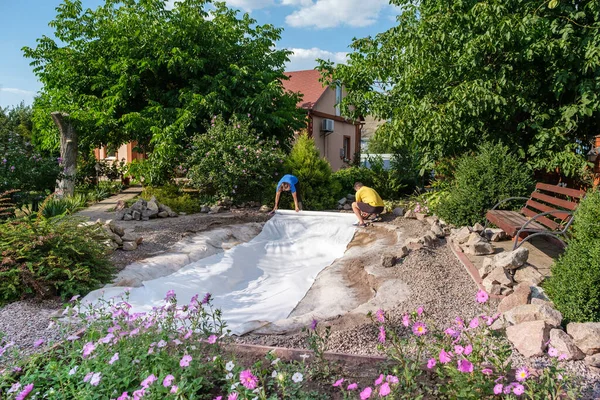 Family roll out a roll of white non-woven geotextile fabric to set up fish pond