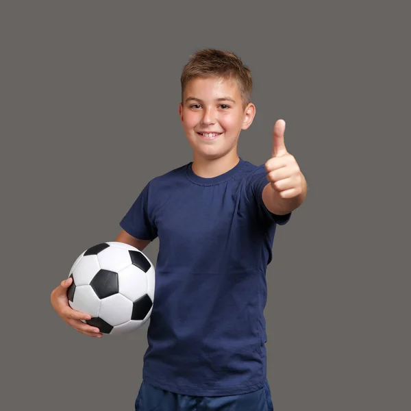 Yakışıklı, gülümseyen beyaz fanatik çocuk futbol topu tutuyor ve başparmaklarını hareket ettiriyor. — Stok fotoğraf
