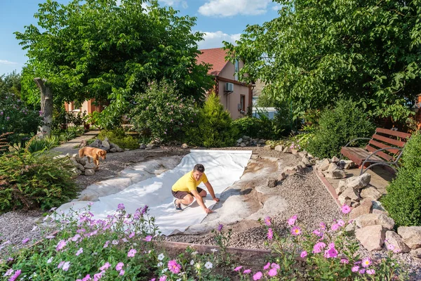 Man roll out a roll of white non-woven geotextile fabric to set up fish pond — Stock Photo, Image