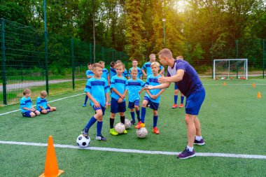 Futbol formalı çocuklar antrenmandaki koçu dinliyorlar. Genç koç, çocuk futbol takımına futbol stratejisini anlatıyor.. 