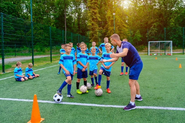 Futbol formalı çocuklar antrenmandaki koçu dinliyorlar. Genç koç, çocuk futbol takımına futbol stratejisini anlatıyor.. 