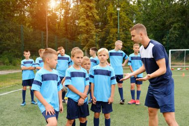 Futbol formalı çocuklar antrenman sırasında koçun açıklamalarını dinlerler. Genç koç çocuk futbol takımına hataları açıklar..