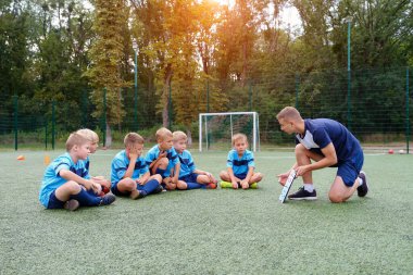 Panolu genç koç, futbol sahasında oynayan çocuklara strateji öğretiyor.
