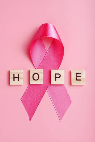 Pink ribbon and wooden letters with word hope on pink background, vertical