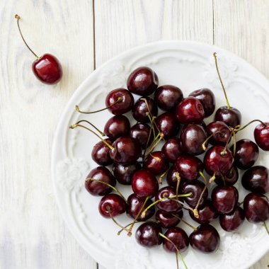 Karanlık tatlı kiraz beyaz bir tabak ve ahşap masa lambası yakın çekim. Üstten görünüm.