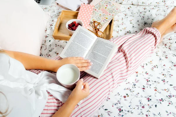 Genç kadın süt içerken evde yatak ve kitap okumak, sayfa görünümü