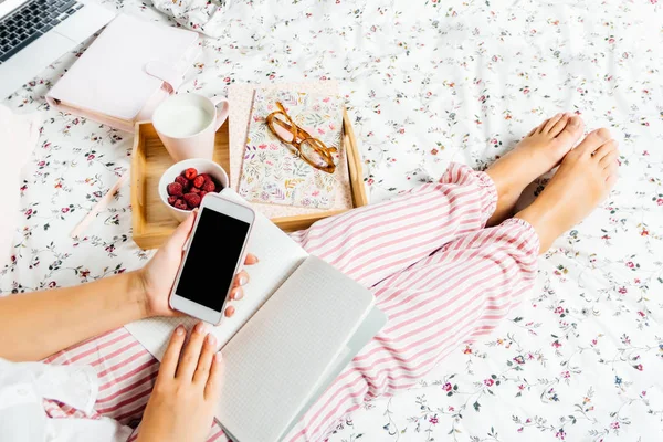 Genç Kadın pijama bir açık not defteri ve telefon evde yatakta üstten görünüm tutar