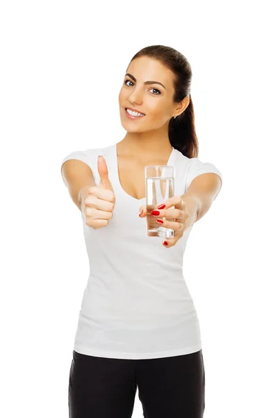 Brunette girl in white t-shirt stretches forward glass of water and shows her thumb up. isolated on white background — Stock Photo, Image