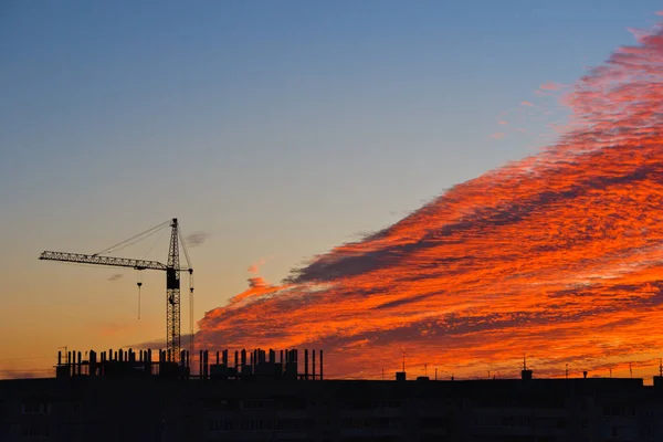 Silueta de la grúa de construcción y la construcción en el fondo del cielo puesta del sol con nubes rojas —  Fotos de Stock