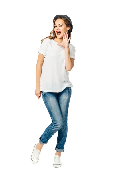 年轻的开朗的女孩穿着牛仔裤 运动鞋和帽子举行她的手掌张开嘴和微笑 隔离在白色背景 — 图库照片