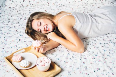 Genç sarışın kız yatakta yatan gülüyor kekler