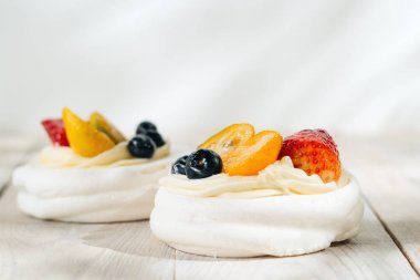 Beyaz ahşap masada krem ve sırlı meyve ile bir pavlovas beze kek