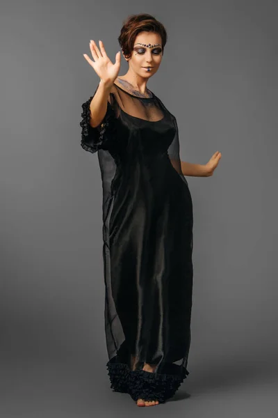 Дівчина в чорній сукні з незвичайним космічним макіяжем витончено танцює позує на сірому фоні — стокове фото