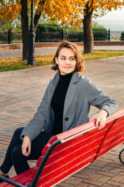 Gri ceketli kız ara sokakta bankta oturuyor.