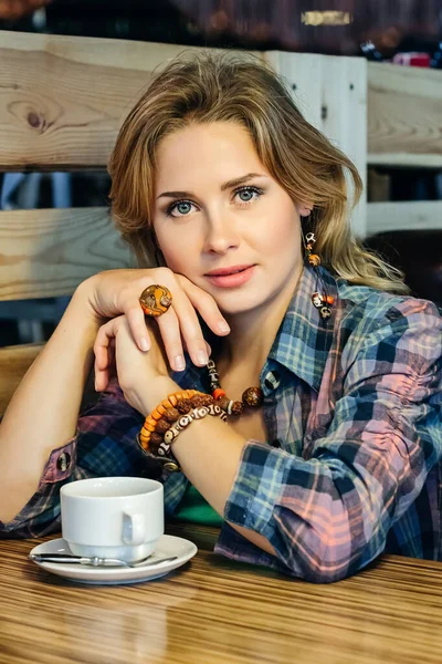 Girl in a plaid shirt sitting in a cafe with a cup of tea — Stock Photo, Image