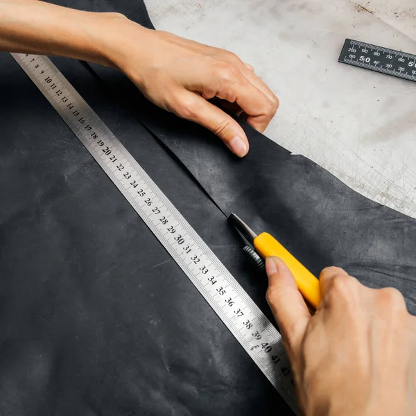 Top view of a persons hands using cutting tool and metal ruler while producing leather goods — Stock Photo, Image