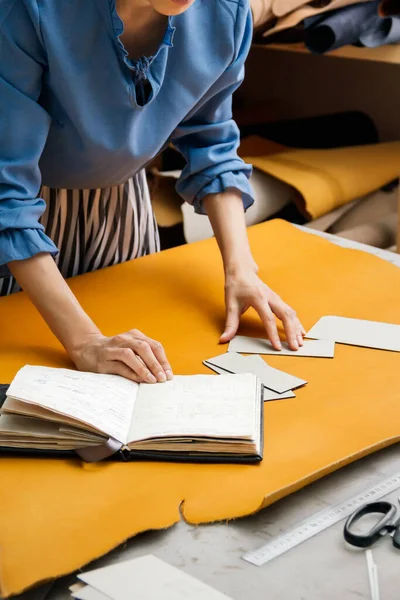 Uma designer feminina estabelece padrões em couro amarelo. a menina olha para o Notebook . — Fotografia de Stock