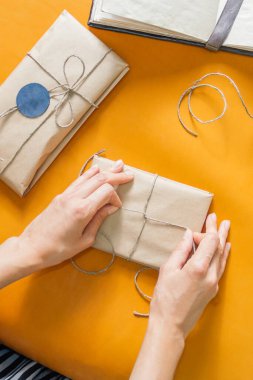 Kadınlar hediye paketliyor. Kağıda sarılmış ve kabataslak sicim görünümlü bir paket.