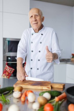 Bir gülümseyen portresi adam mutfakta yemek için hazırlanan yaşlı. Büyükbaba gri saçlı sebze Dilimleme.