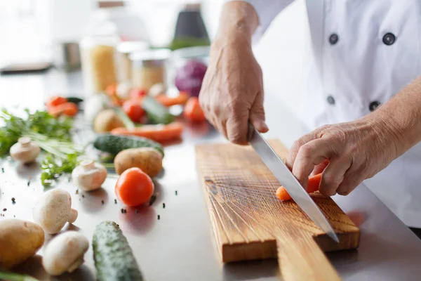 Manos masculinas con un cuchillo cortando zanahorias en la cocina. Un concepto de cocina. Hortalizas — Foto de Stock