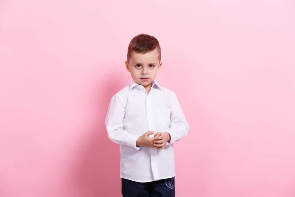 Um menino adorável em uma camisa branca em um fundo rosa . — Fotografia de Stock