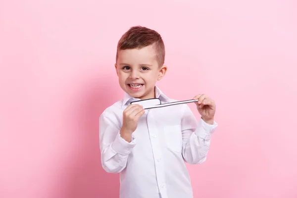 Um menino feliz escovando os dentes segurando uma grande imagem de papel de um dente e escova de dentes em um fundo rosa — Fotografia de Stock
