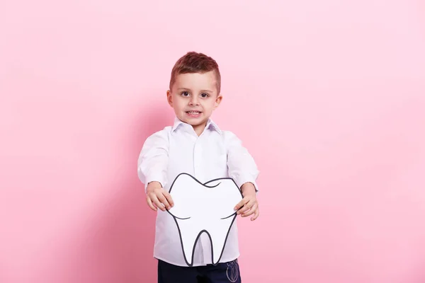 Um menino com um dente de papelaria num fundo cor-de-rosa. Conceito de saúde — Fotografia de Stock