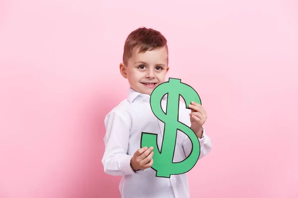 Un niño feliz sostiene un falso dólar verde americano sobre un fondo rosa . — Foto de Stock