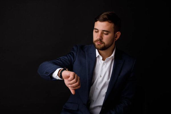Portrait of a young and thoughtful businessman in a suit looks at his wristwatch on a black background. The concept of a successful business.