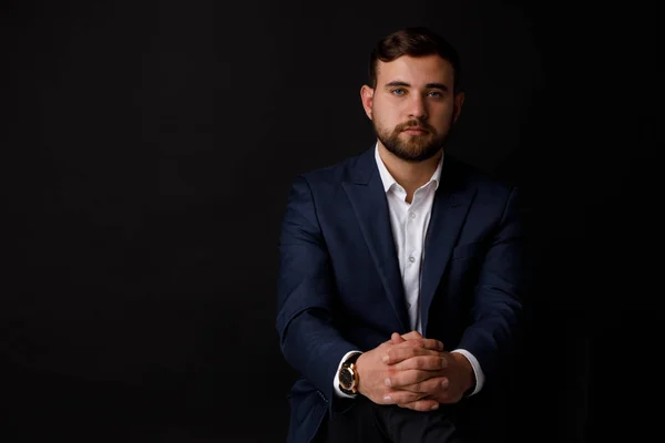 Close-up portrait of an attractive businessman with a beard in a formalwear on a black background. The concept of a success.