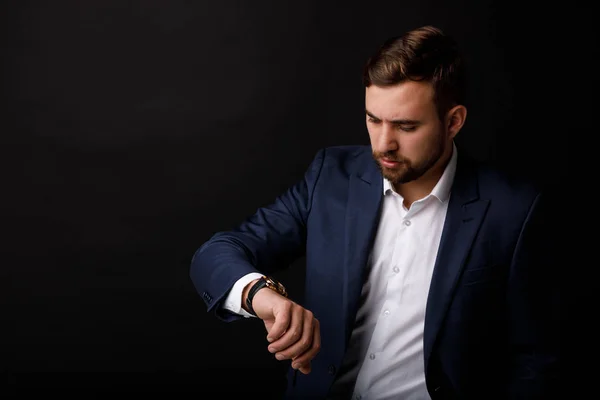 Portrait Young Thoughtful Businessman Suit Looks His Wristwatch Black Background — Stock Photo, Image
